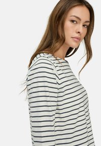 Gestreiftes Langarmoberteil in Weiß mit navyblauen Horizontalstreifen. Verfügt über einen Rundhalsausschnitt und einen weichen Stofftextur.