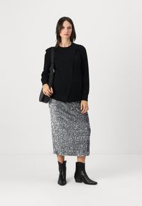 Maglione nero in maglia, gonna maxi in paillettes argento con arricciature, stivaletti neri alla caviglia e borsa a tracolla. Design semplice e funzionale.