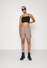 Top court noir, pantalons courts à carreaux marron clair et bottes noires à lacets avec une semelle épaisse. Matière couleur peau et design minimaliste.