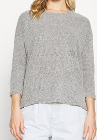 Ljusgrå stickad tröja med lös passform, rund halsringning och trekvartslånga ärmar. Strukturerat mönster med ribbade muddar.