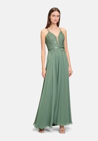 Langes grünes Kleid mit tiefem V-Ausschnitt, verziertem Oberkörper und fließendem Rock. Verfügt über Spaghetti-Träger und filigrane Perlenverzierungen.