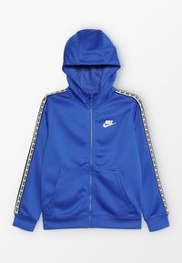 Sudadera con capucha azul con cremallera, fabricada en tela suave, que presenta una capucha, bolsillos laterales y una cinta de color negro y blanco en contraste a lo largo de las mangas con el logo de Nike.