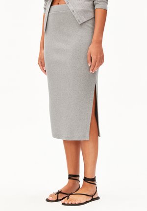 Femme portant une jupe midi en maille grise avec une fente latérale, associée à des sandales plates noires à lanières et un cardigan gris assorti.