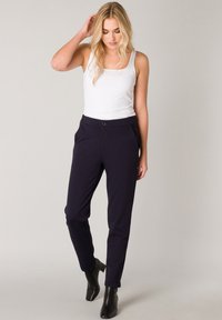 Witte tanktop met een vierkante halslijn, gecombineerd met marineblauwe taperende broek met een knoopsluiting en zijzakken. Zwarte enkellaarsjes.