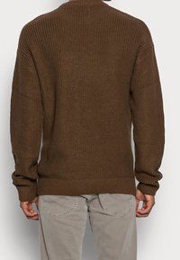 Brun stickad tröja med ribbat mönster, avslappnad passform och långa ärmar; har en rundad halsringning samt elastiska fållar och ärmslut.