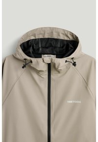 Beige regnjakke med justerbar hætte, sort lynlås og "TRETORN" logo på brystet.