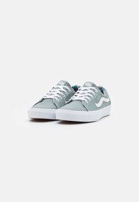 Light green canvas sneakers with white laces and rubber soles. Features white logo and multicolored patterned lining. Low-profile design.