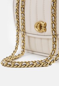 Kremfarvet læderhåndtaske med lodret syning, guldfarvet drejelås og guldkæde-rem flettet med matchende læder.