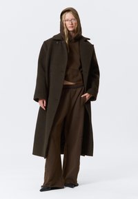Brown oversized wool coat with large lapels, paired with matching brown cropped hoodie and wide-leg pants. Slim black shoes complete the look.