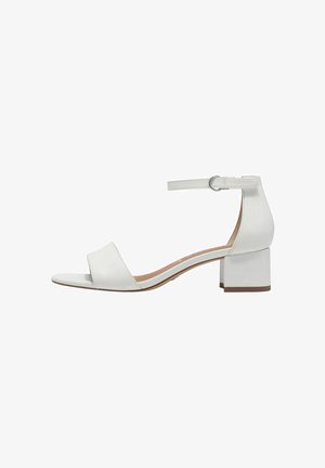 White heeled sandals with a block heel, open toe, and ankle strap. Smooth synthetic material with minimalistic design and brown sole.