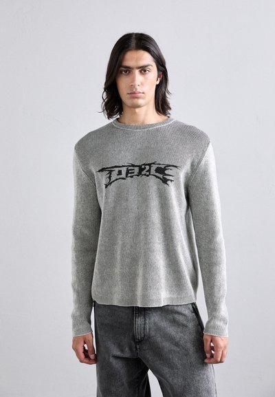 Maglione grigio a coste con maniche lunghe, scollatura rotonda e scritte grafiche nere sul petto. Abbinato a pantaloni grigio scuro.