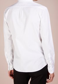 Witte lange mouwen shirt met een button-down kraag, met een rechte achterkant en manchetten die met knopen zijn vastgemaakt. Gladde katoenen textuur.