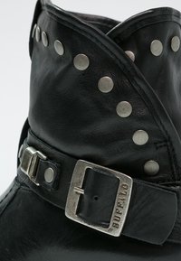 Czarny skórzany botek za kostkę z srebrnymi ćwiekami wzdłuż kołnierza oraz metalową klamrą. Gładka tekstura z założonym detalem.