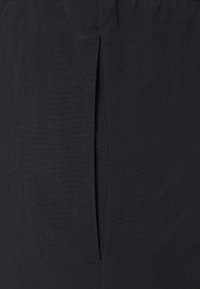 Pantaloni neri con una texture liscia, vita elastica e dettaglio con spacco laterale, progettati per comfort e facilità di movimento.