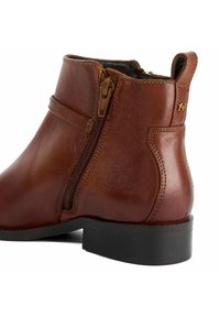 Bottine en cuir marron avec fermeture éclair sur le côté, talon empilé et texture lisse. Présente un accent de logo et des coutures renforcées le long des seams.