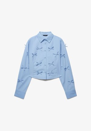 Hellblaues, kurz geschnittenes Hemd mit Knopfkragen, langen Ärmeln und dekorativen Schleifen vorne und an den Ärmeln. Glatte Textur.