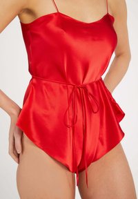 Red satin romper with a fitted bodice, adjustable spaghetti straps, and a cinched waist featuring a tied drawstring. Flared shorts design.