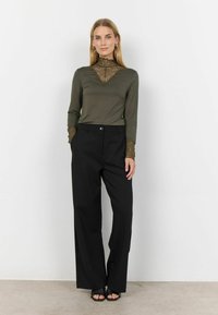 Maglione verde oliva a maniche lunghe con dettagli in pizzo sul collo e sui polsini, abbinato a pantaloni neri a vita alta e larghi. Sandali neri.