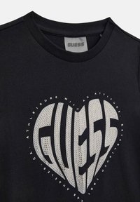 Μαύρο βαμβακερό T-shirt με μεγάλο ασημένιο λογότυπο σε σχήμα καρδιάς με υφασμάτινη υφή και λευκό κείμενο. Στρογγυλή λαιμόκοψη με εκτεθειμένες ραφές.