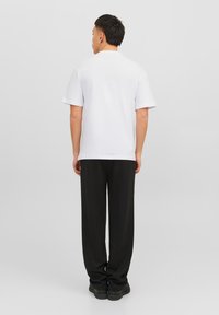 White cotton t-shirt with short sleeves and a crew neckline, paired with loose-fitting black pants. Minimalistic design, solid colors.