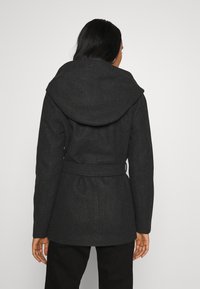 Abrigo de mezcla de lana negra con capucha sobredimensionada, cinturilla ajustable y mangas largas; textura suave y corte entallado. Se muestra vista trasera.