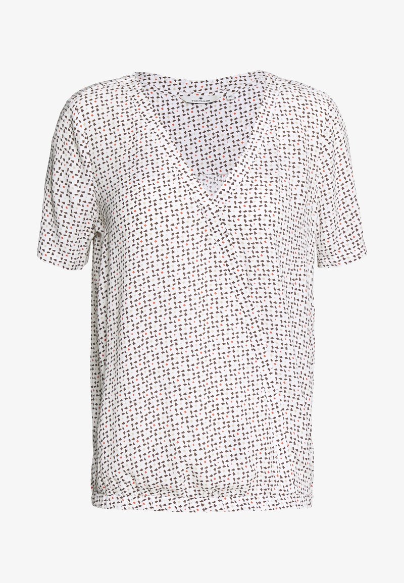 Haut blanc à manches courtes avec un col en V, un design portefeuille et un motif géométrique dispersé en marron et rouille. Texture de tissu douce.