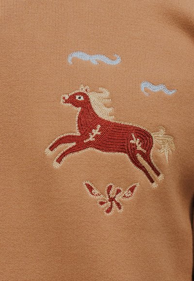 Καφέ ύφασμα με κεντημένο κόκκινο άλογο που πηδά, εκρού χαίτη και ουρά, μπλε ραμμένα σύννεφα από πάνω και λουλουδένιο σχέδιο κάτω.