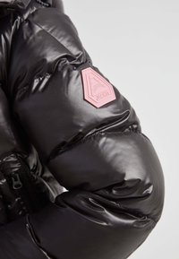 Chaqueta acolchada negra con un acabado brillante, que presenta un parche de logo hexagonal rosa en la manga izquierda y detalles en negro en los cremalleras.