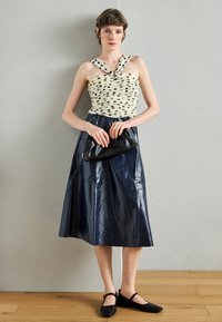 Bluza crem deschis cu buline și bretele încrucișate, asortată cu o fustă A-line lucioasă în bleumarin închis. Poșetă neagră de mână și pantofi comozi completează ținuta.