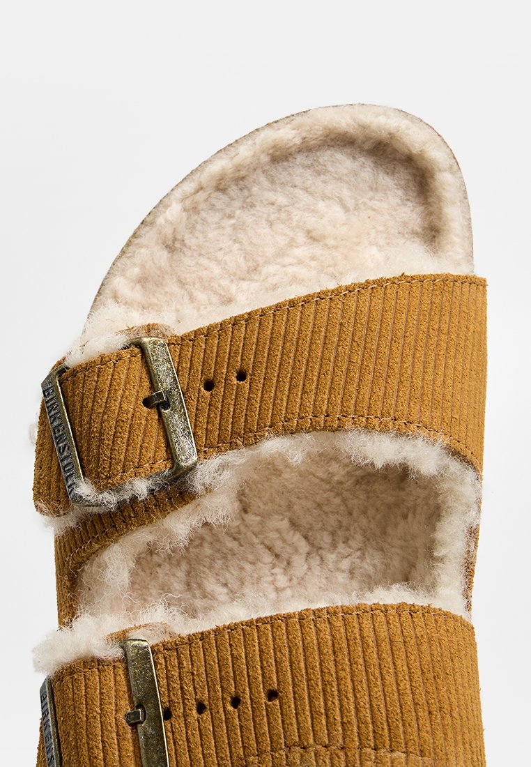 Braune Wildleder-Sandale mit zwei verstellbaren Schnallenriemen und weichem weißen Fleece-Futter für zusätzlichen Komfort.