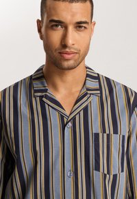 Camisa de pijama a rayas con cuello, que presenta rayas verticales azules, marino y amarillas, bolsillo frontal y dos botones en la tapeta.