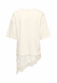 Haut blanc oversize à manches courtes avec un ourlet en dentelle asymétrique qui s'étend sous le dos.