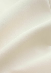 Glattes, cremefarbenes Stofffalten mit einer weichen, feinen Textur und dezenten Lichtschatten, die sanfte Kurven betonen.