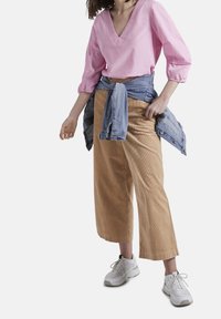 Blusa rosa chiaro a scollo a V con maniche a tre quarti, abbinata a pantaloni wide-leg in corduroy beige. Giacca di denim chiaro legata in vita; sneakers bianche.
