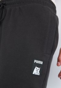 Sorte sweatpants lavet af blødt materiale, med et hvidt kattegrafiklabel og en snøre i taljen til justerbar pasform.