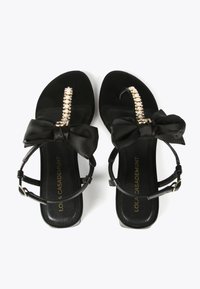 Black sandals with a bow detail, jewel accents on the toe strap, and a sleek, flat sole. Strap design includes an adjustable buckle.