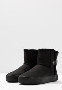 Bottines noires en cuir texturé avec une doublure en fausse fourrure, dotées d'une semelle en caoutchouc plate et d'une boucle décorative sur le côté.