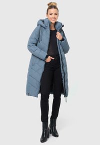 Gaiši zils quilted garais pūkains mētelis ar kapuci, priekšējo rāvējslēdzēju un saites. Valkāts virs melnas augšdaļas un apvienots ar melnām biksēm un potīšu zābakiem.