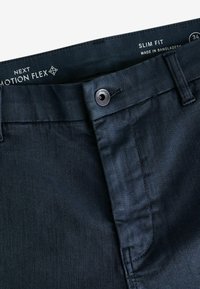 Pantalones oscuros ajustados de color azul marino, hechos de una suave tela texturizada, con cierre de botón y una etiqueta que dice "Next Motion Flex."