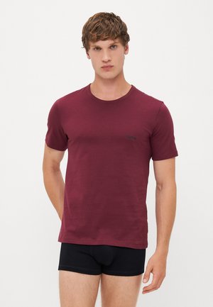 Tricou scurt cu mânecă în culoarea burgundă, cu guler rotund, realizat dintr-un material moale; are un mic logo negru pe piept. Asortat cu pantaloni scurți negri.