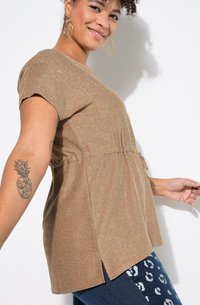 Bruine, glinsterende top met korte mouwen, een verzamelde taille en zijsplitten, gecombineerd met donkere jeans met een wit luipaardprintpatroon.
