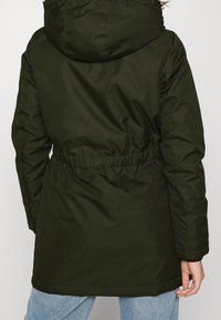 Parka olive verte avec une taille cintrée, capuche et texture douce. Présente une finition lisse et des manches longues avec des poignets élastiques.