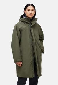 Green, waterproof parka with a hood, featuring a zip closure and snap buttons, textured fabric, and side pockets.