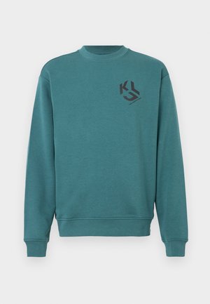 Τιρκουάζ φούτερ φτιαγμένο από μαλακό ύφασμα, με στρογγυλή λαιμόκοψη, μακρυά μανίκια, ριμπ μανσέτες και μαύρο λογότυπο στο στήθος.