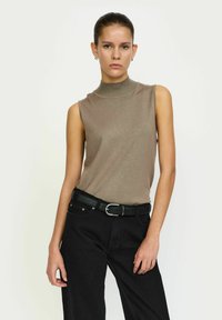 Top s bez rukava u svijetlosmeđem rebrastom pletenju, u kombinaciji s crnim trapericama visokog struka i crnim remenom s srebrnom kopčom.