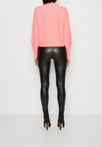 Světle růžový krátký svetr v kombinaci s lesklými černými legínami z umělé kůže a černými kotníkovými botami na podpatku. Hladká textura s žebrovanými detaily.