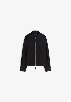 Schwarze Zip-Jacke mit flachem Kragen, langen Ärmeln und slim fit. Mit einem metallischen Reißverschluss und subtiler Textur.