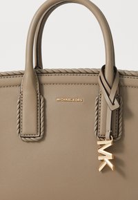 Beige leather handbag with braided handles, gold-tone hardware, and a hanging MK logo charm. Features a smooth texture and clean design.