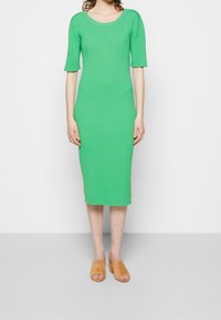 Robe en tricot côtelé verte à manches courtes, dotée d'un col rond et d'un ourlet mi-long. Associée à des sandales plates camel.