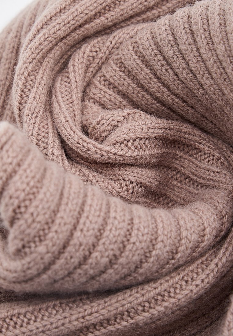 Z dzianiny szalik w jasnoróżowej wełnie, z prążkowaną fakturą i miękkim, lekkim wyglądem, zwinięty w luźny spiralkę.